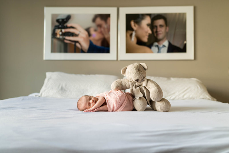 newborn posed on a bed with a stuffed bear