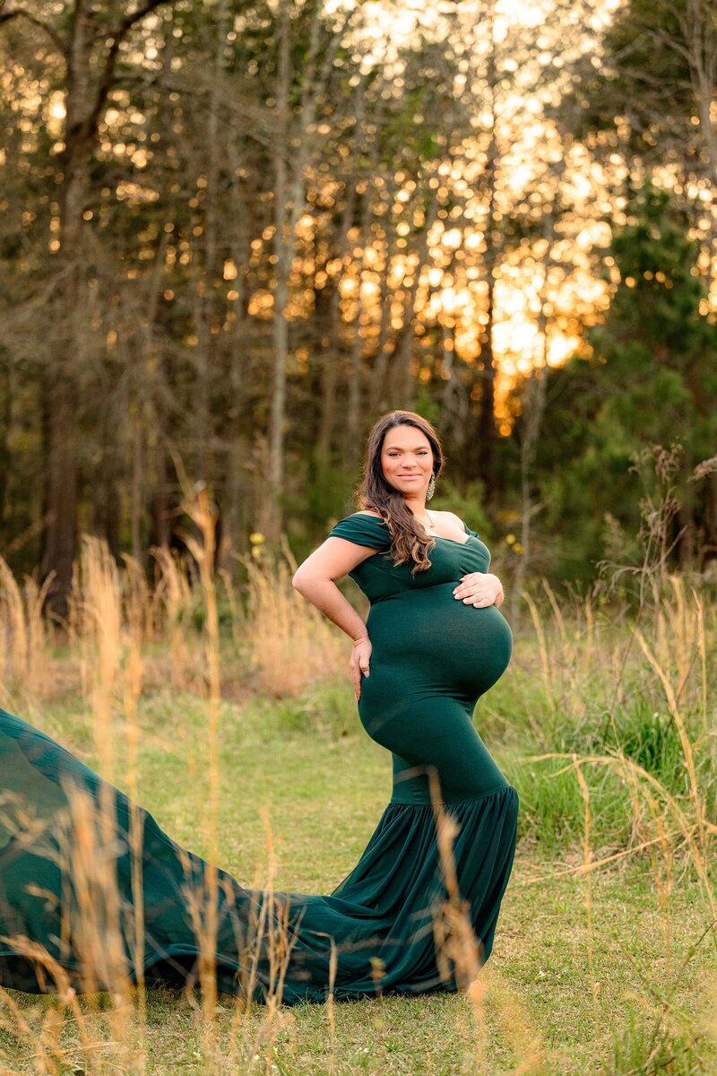 A Charlotte mom is posed and a dark green Hunter dress from the maternity closet with the train flowing in the Wind