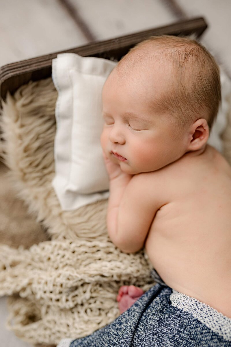 Overhead profile photo of a newborn baby boy laying on a bed with his hand gently underneath his cheek where you can see all of his tiny details of his eyelashes nose and lips