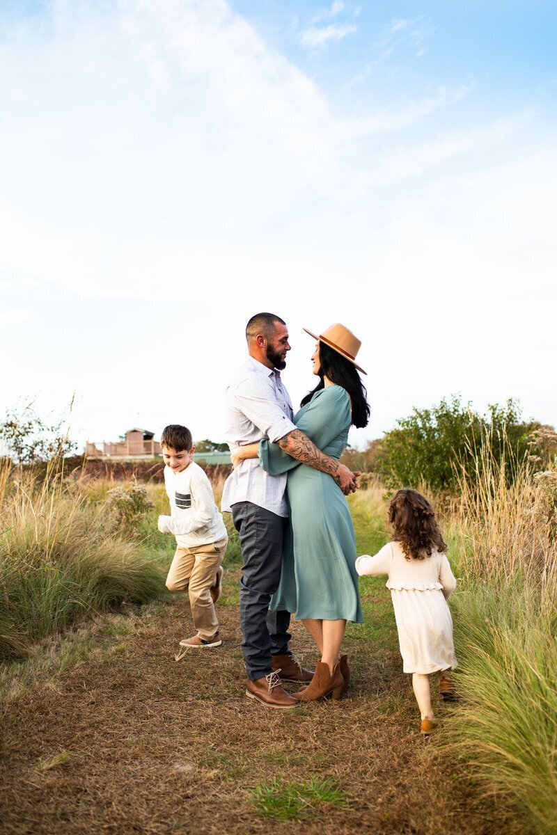 Parents looking at each other and kids running around, by family photographers new jersey