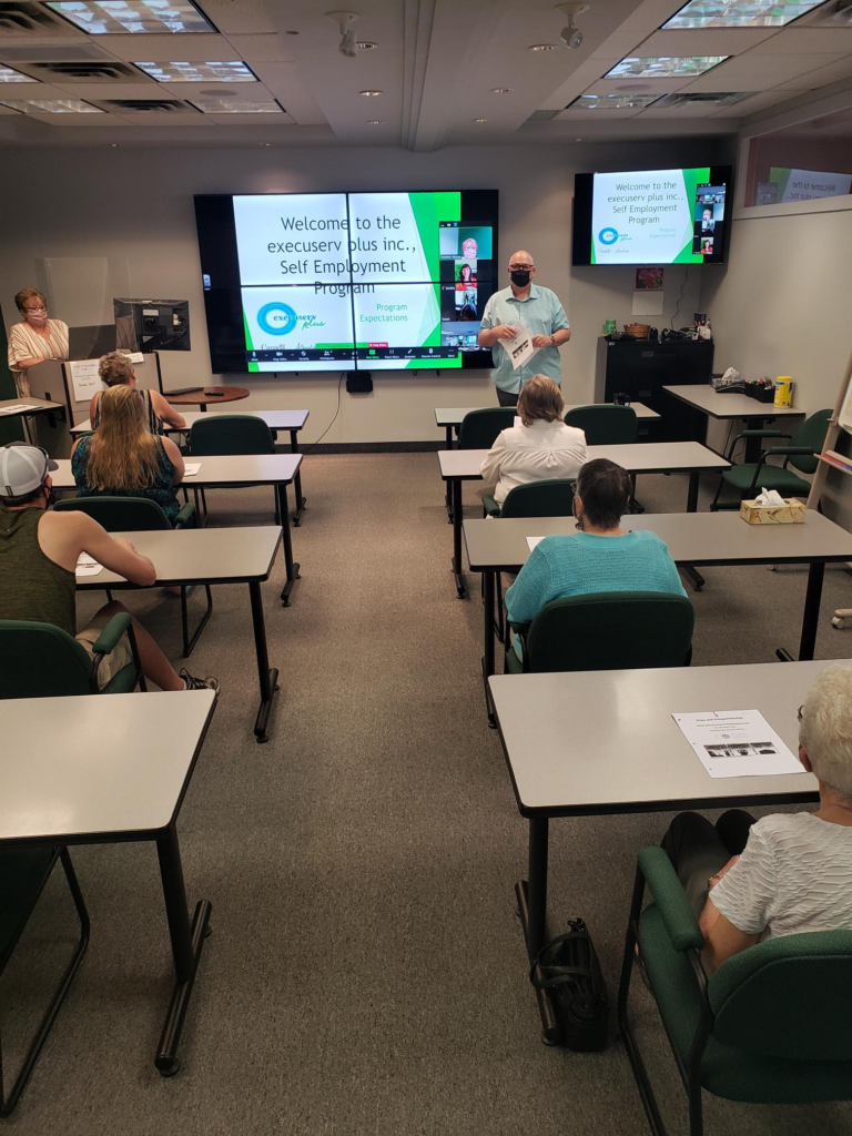 Classroom at execuserv plus inc with an instructor at the front of the class. Teaching to entrepreneurs in class and virtually.