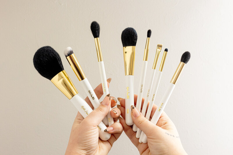 Two hands holding a group of white makeup brushes