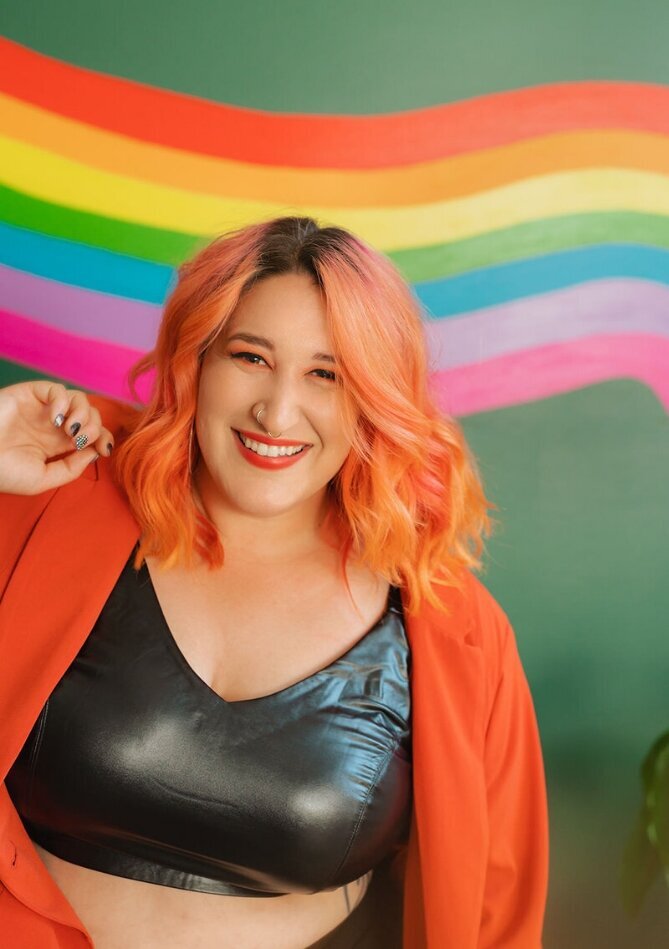 A person smiling in front of a rainbow painted wall.