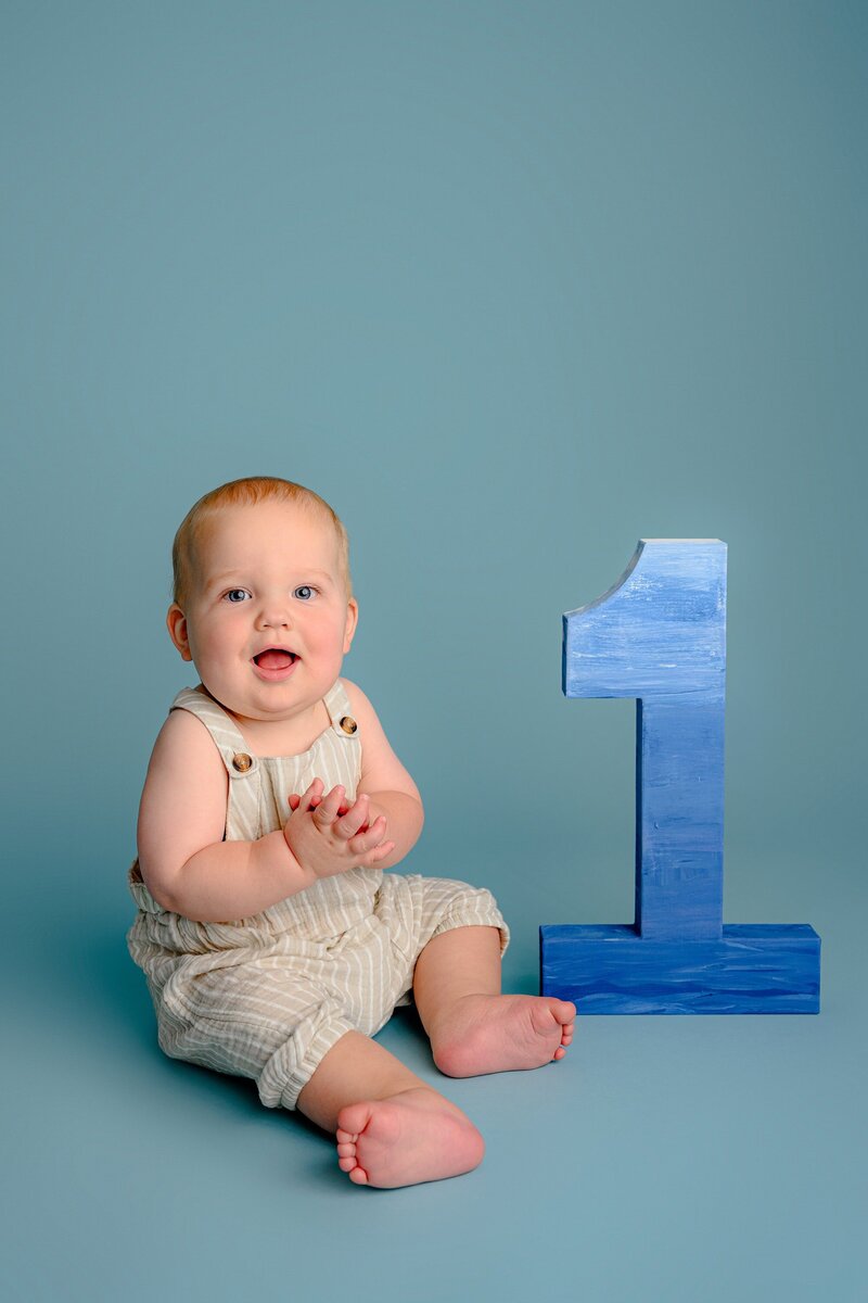 little boy claps as he sits on a blue background