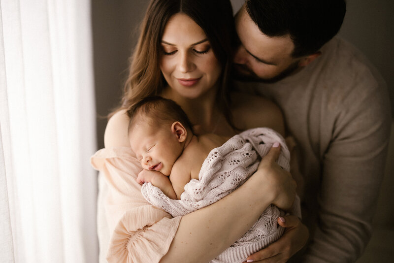 A mother and father holding a newborn baby in their arms during a newborn photoshoot with aimee kelly photography in taranaki