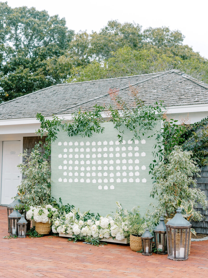 Outdoor image of a large light green seating chart display surrounded by greenery and floral arrangements