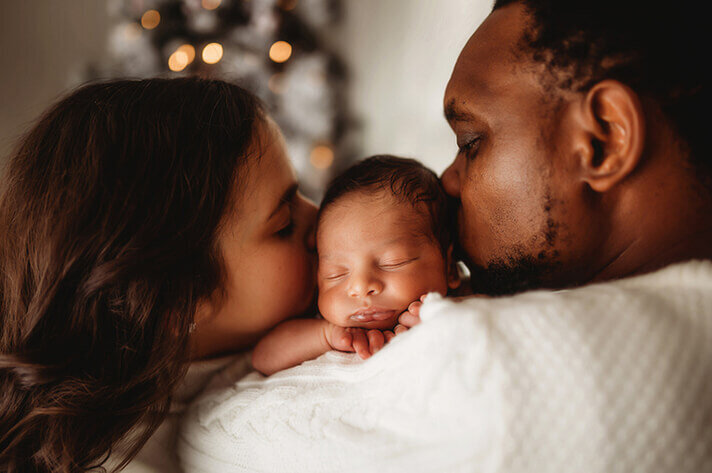 Parents kiss their infant during Newborn Photo Session in Asheville, NC.