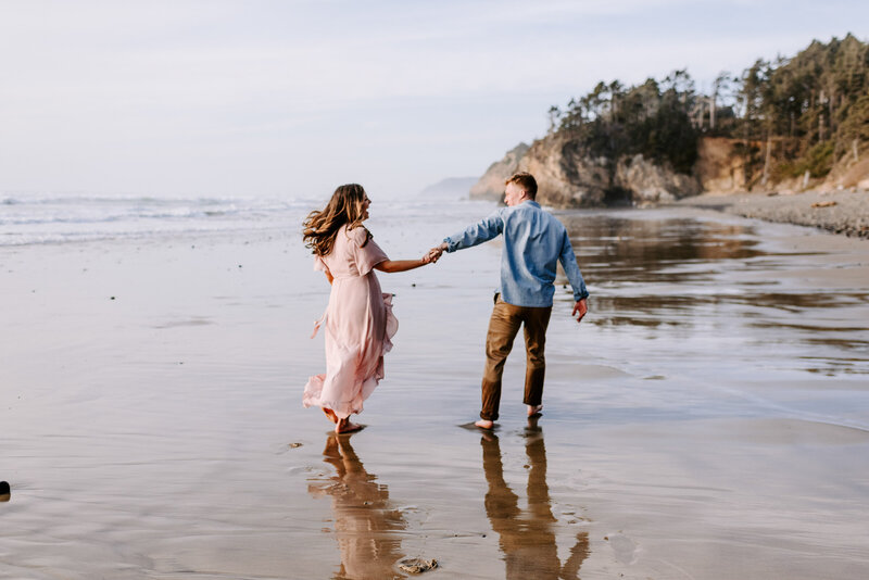 man and woman smiling and holding hands while walking on the beach