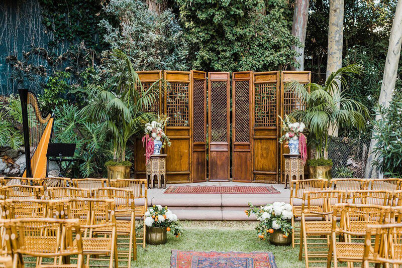 An outdoor wedding ceremony set up featuring wicker chairs, a stone platform with a