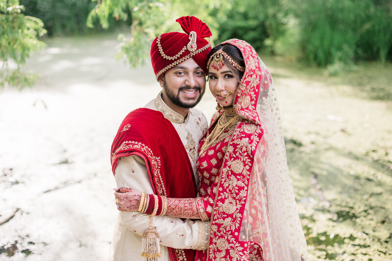 Portrait of bride and groom wearing a red saree wedding dress and lengha