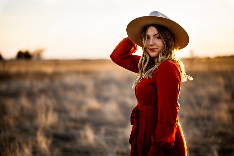 Girl in western dress holds onto her hat as the wind blows her hair in a field