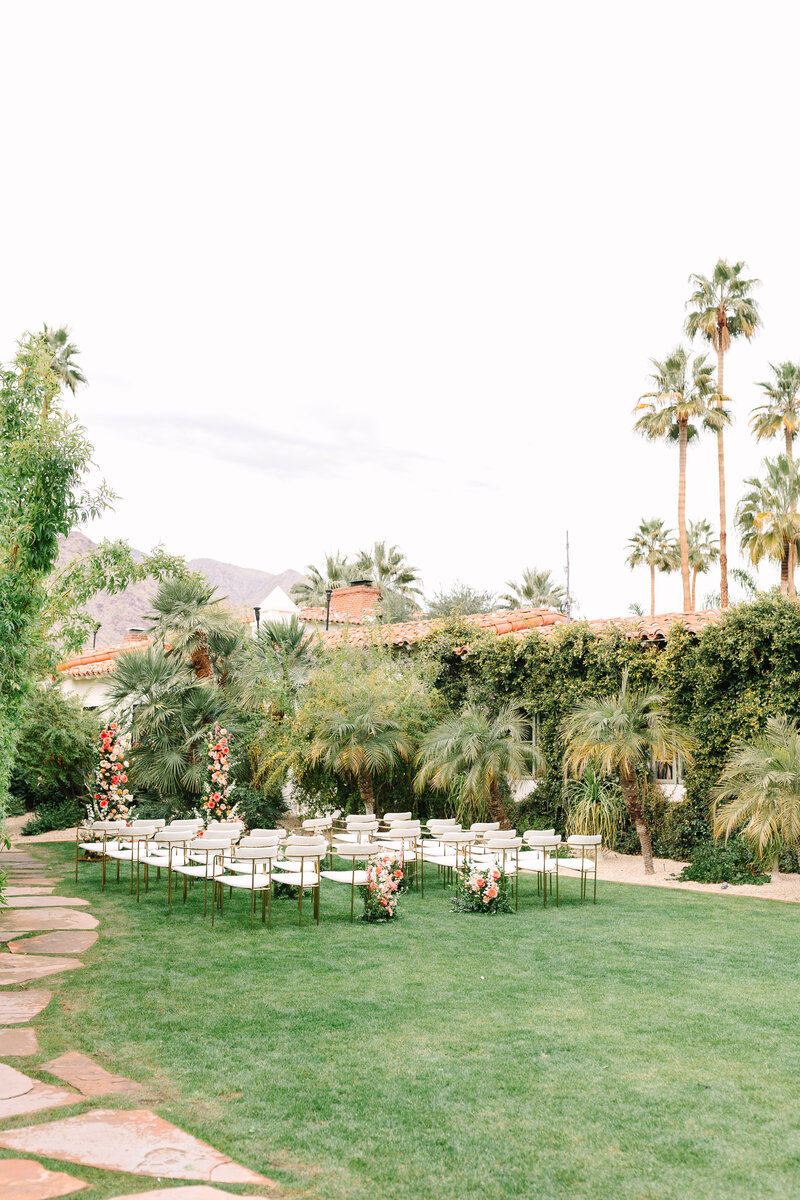outside wedding ceremony set-up in california with green grass and palm trees in background.
