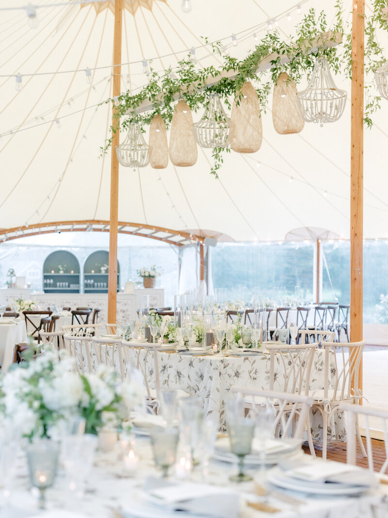 Wedding reception tables with floral tablecloths and greenery hanging from under the reception tent