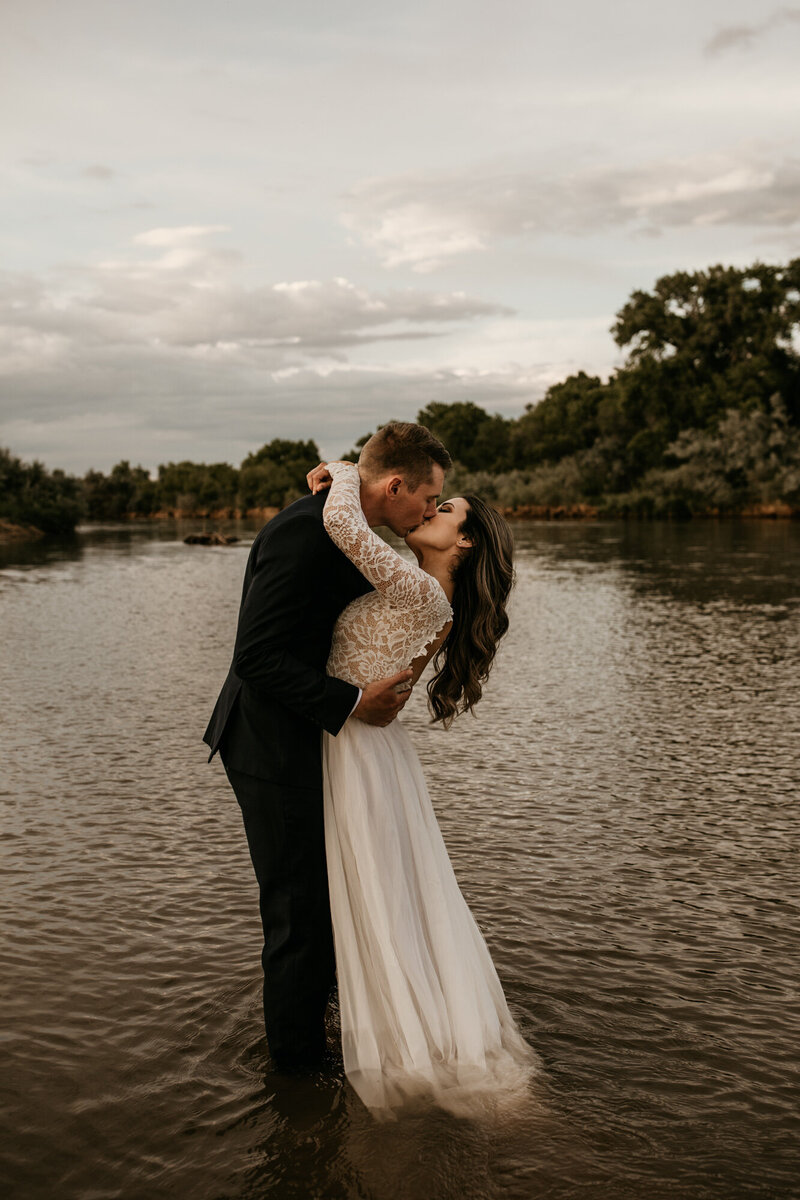 bride and groom kissing each other in the middle of a river in wedding clothes