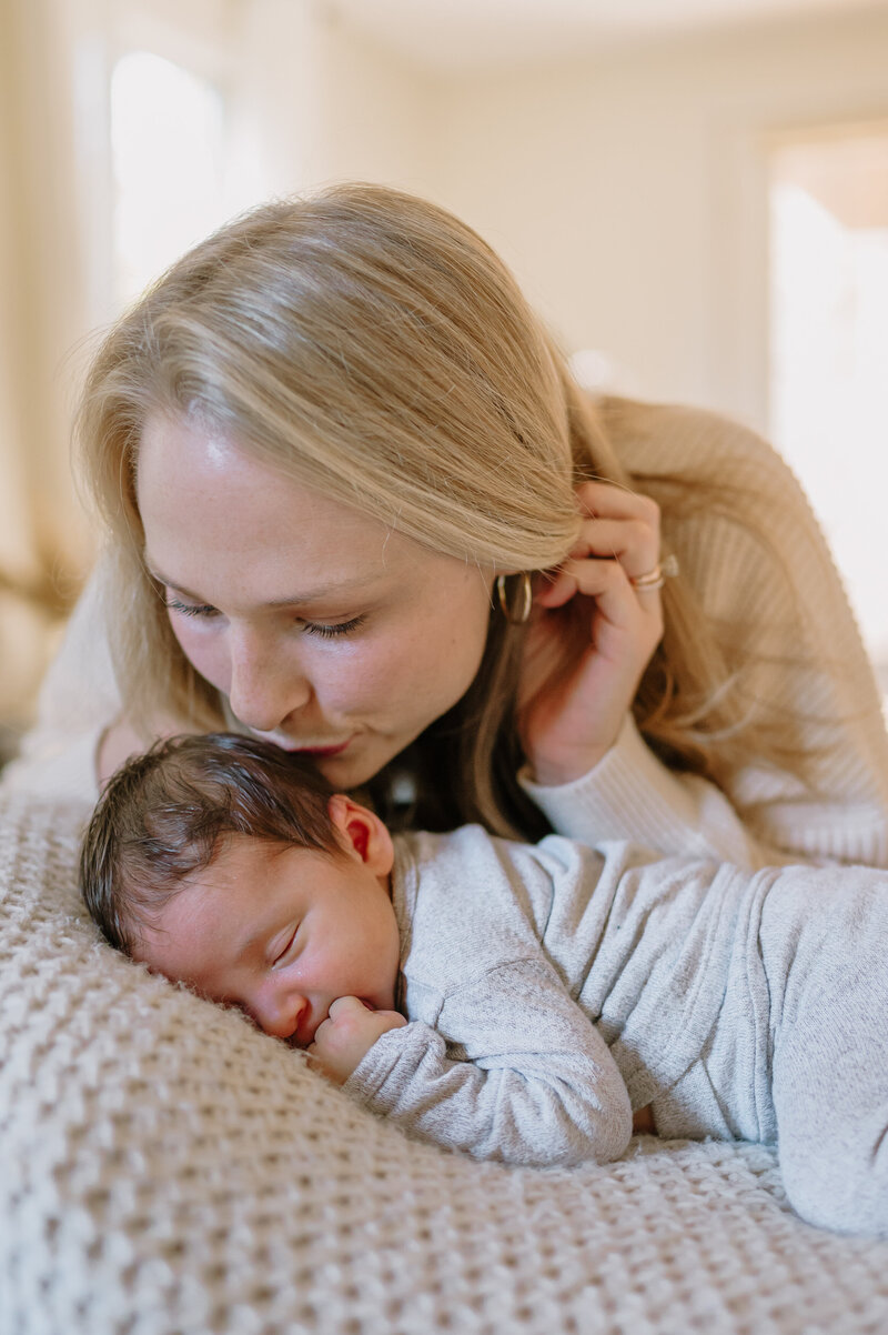 woman kissing top of baby's head laying on a blanket