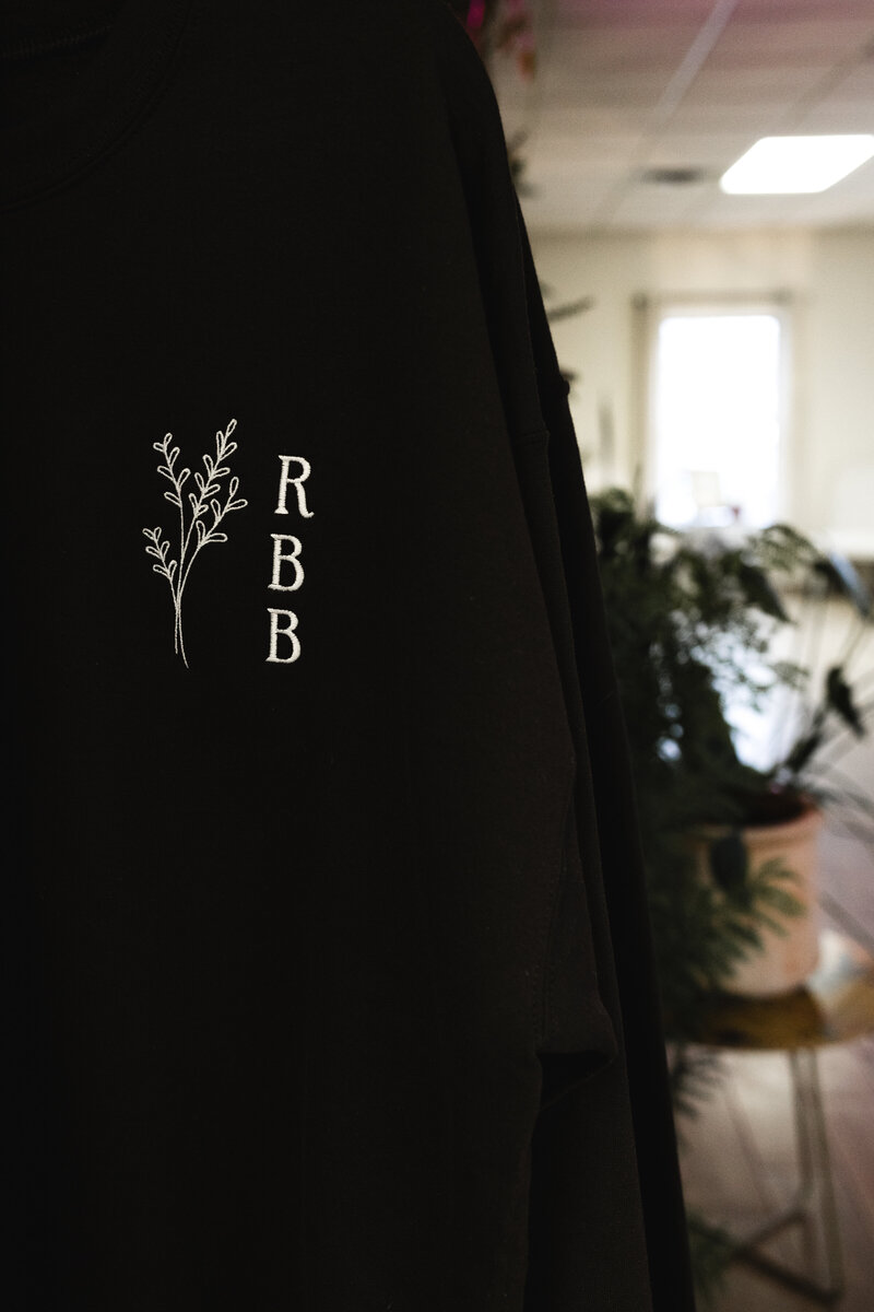 Raw Beauty Bar black sweater with plants in background