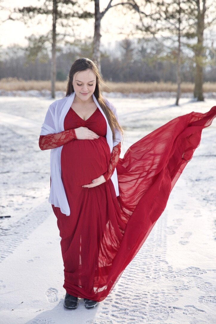 Pregnant mother standing in the snow and looking at her belly at a maternity photo session in westerville ohio