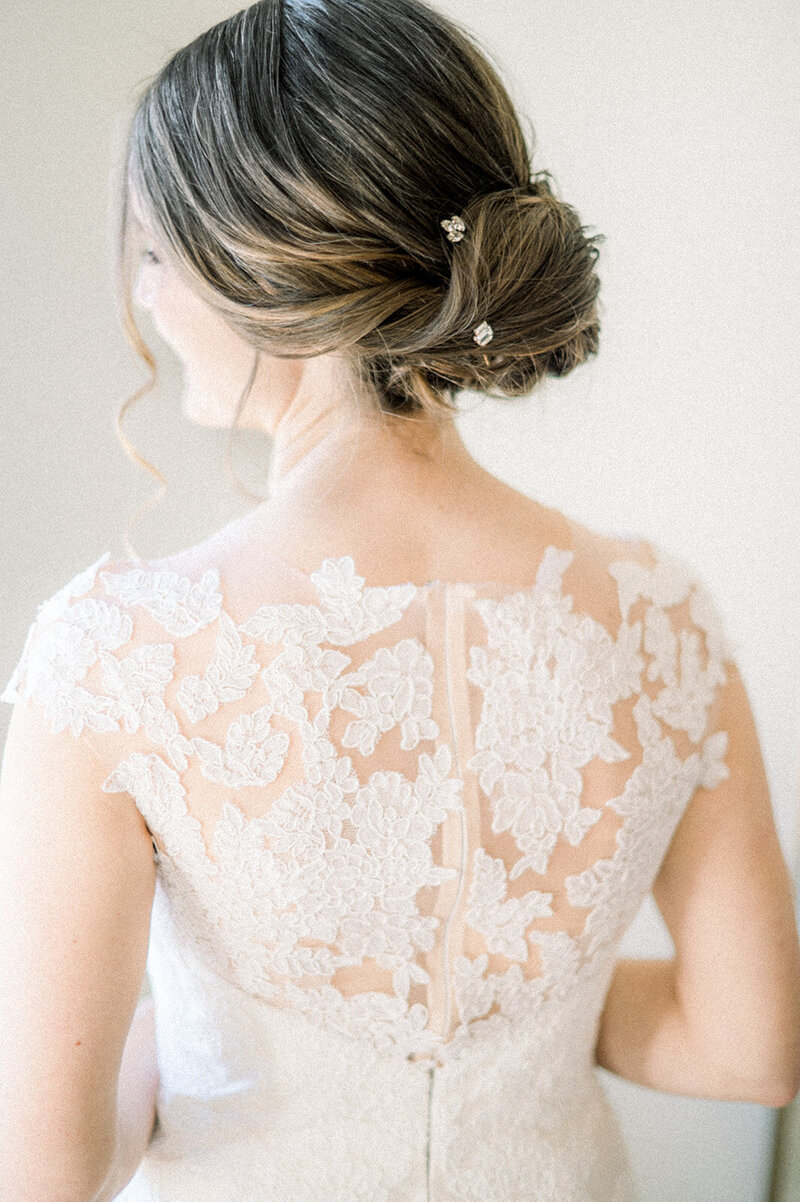 bride getting ready by a window on her wedding day with an elegant updo and her back to the camera looking out the window at northstar gatherings weddings and events venue by colorado wedding photographer kari joy photography