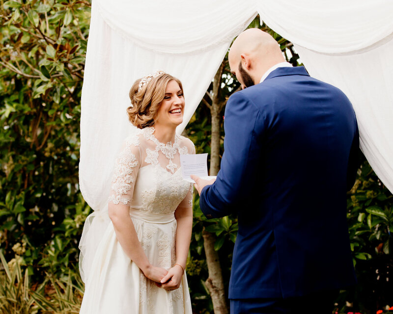 Bride smiles while groom reads his vows