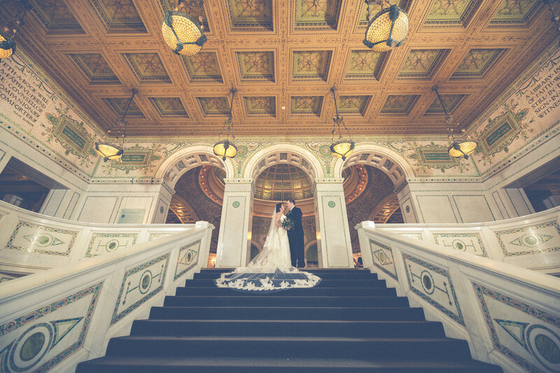 A bride and grooms on the steps of the luxury Chicago Cultural Center with beautiful architecture and archway entrance behind them.