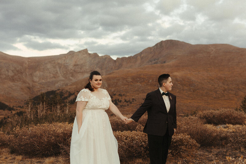 A couple stands with the Colorado mountains behind them as a Colorado wedding photographer takes their picture.