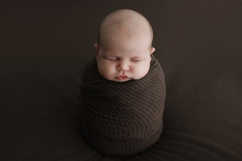 newborn-baby-boy-wrapped-in-brown-textured-wrap-sleeping-with-slight-smile