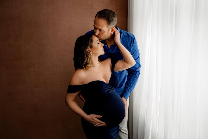 expectant couple embraces and leans together with mom wearing  navy off shoulder maternity dress