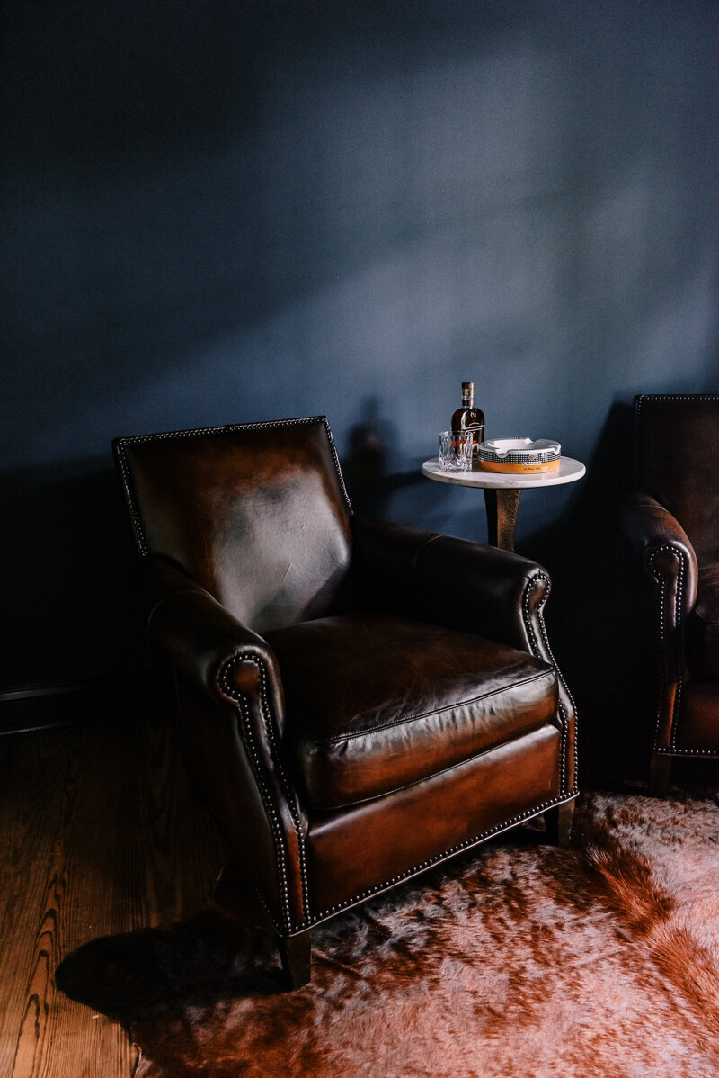 Moody navy blue cigar room with cowhide and cognac leather chairs with draping soft light