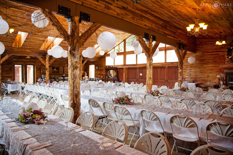 Long rows of white tables inside Mountain View Ranch for a rustic wedding reception in a Colorado barn