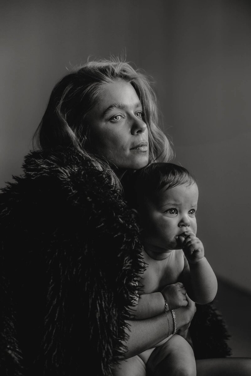 Emotive motherhood photography capturing a mother holding her baby in soft indoor light.