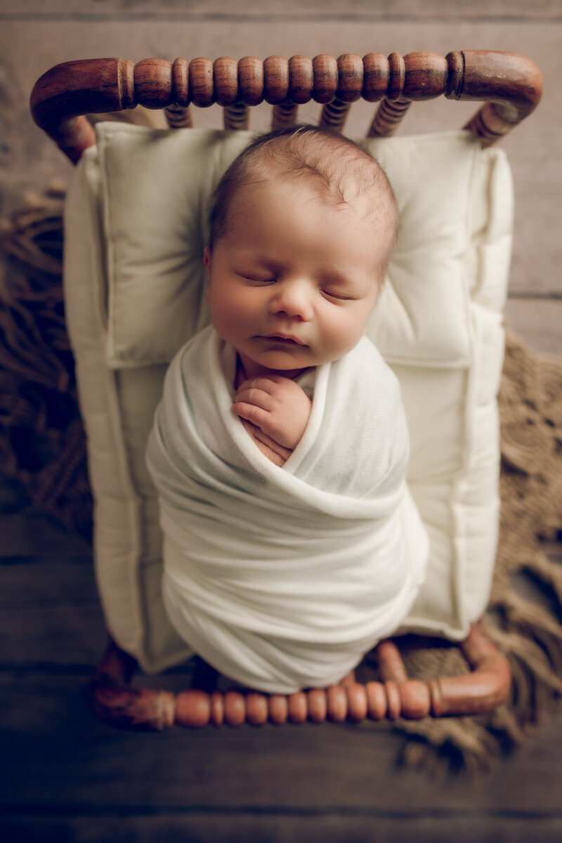photo of a newborn baby boy wrapped in white in a tiny bed during his newborn studio session in Tucson