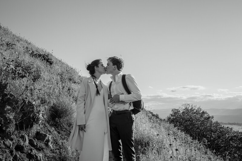 Bride and groom kissing on the side of a grassy mountain