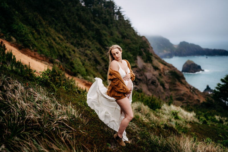 Maternity Photographer, an expectant mother stands on a mountainside trail near the ocean