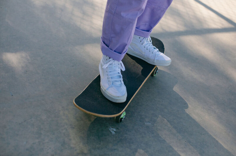 Close up of someone in purple pants and white shoes skateboarding.