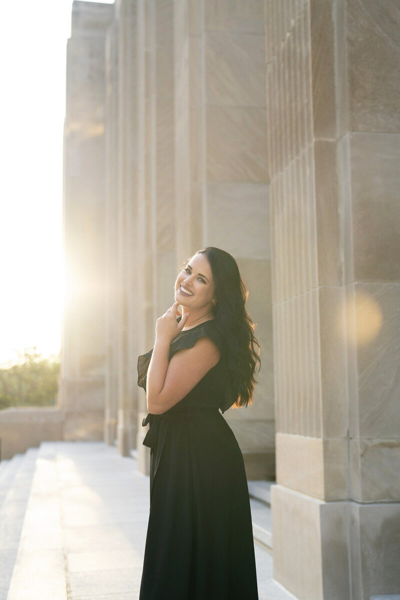 headshot of destination wedding photographer, Kaitlyn Cole, holding her camera and wearing a classic black dress