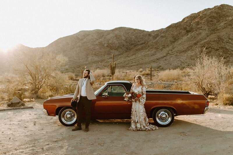 bride and groom posing in the desert in front of a car