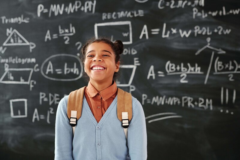 Student standing in front of chalkboard, smiling