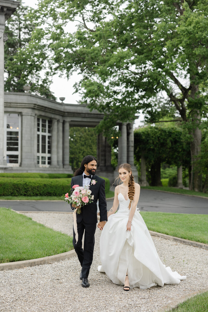 photo of bride and groom walking down gravel pathway in front of estate home