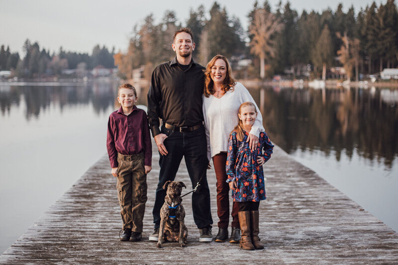 Family, father, mother, children son and daughter, posed on a dock  with their dog all looking happy