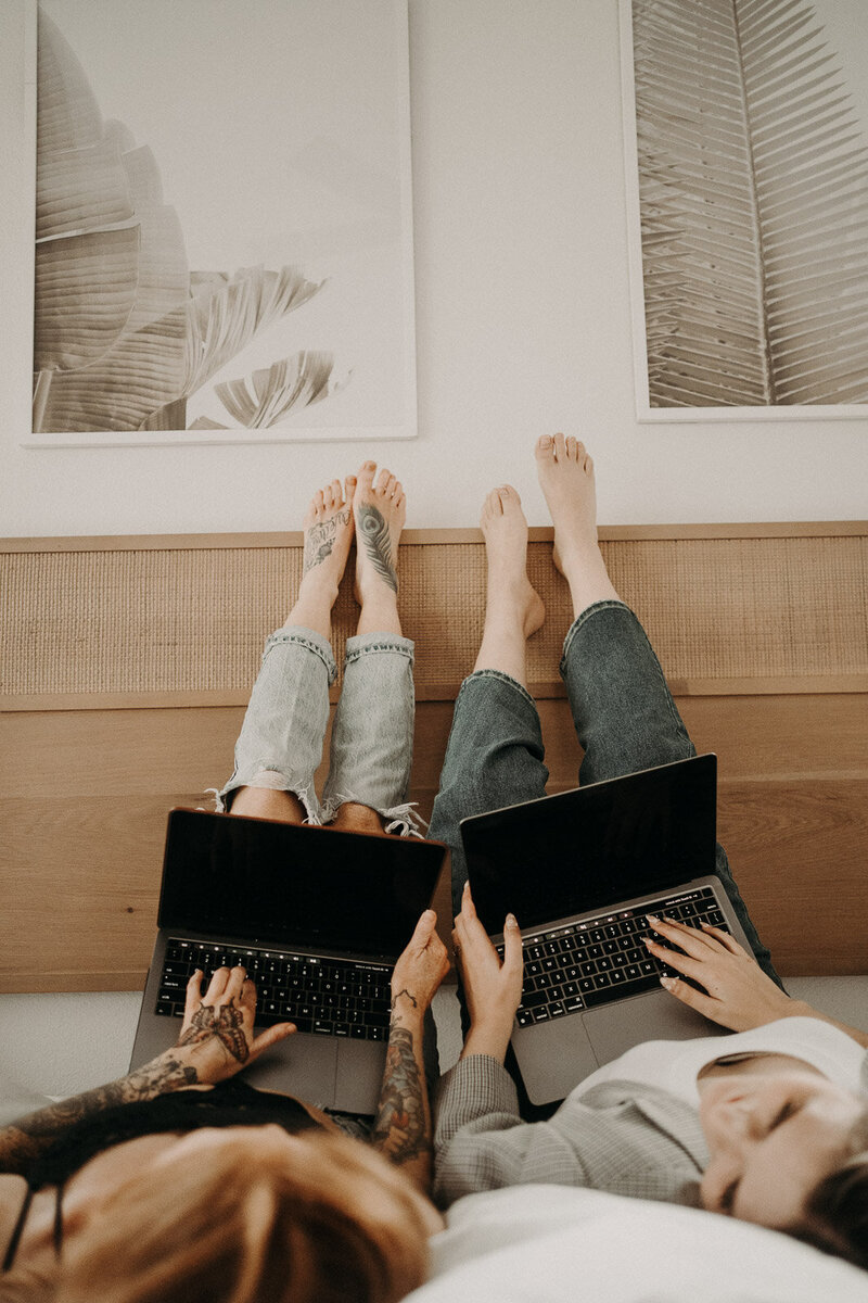 two girls laying on the floor with their legs up the wall and laptops on their lap
