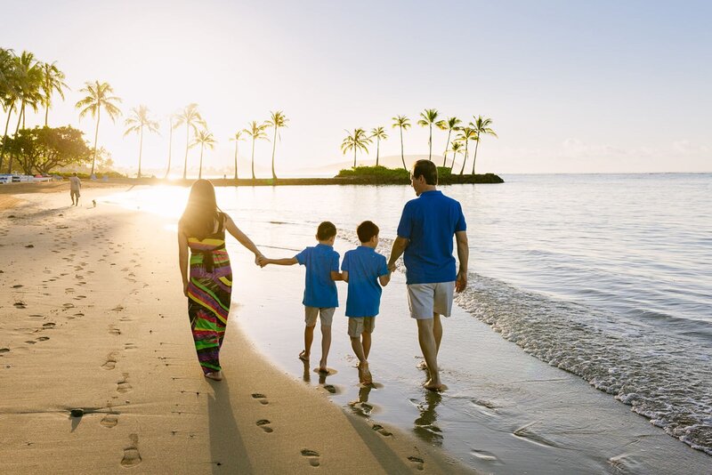A family with two boys hold hands walking along the beach.