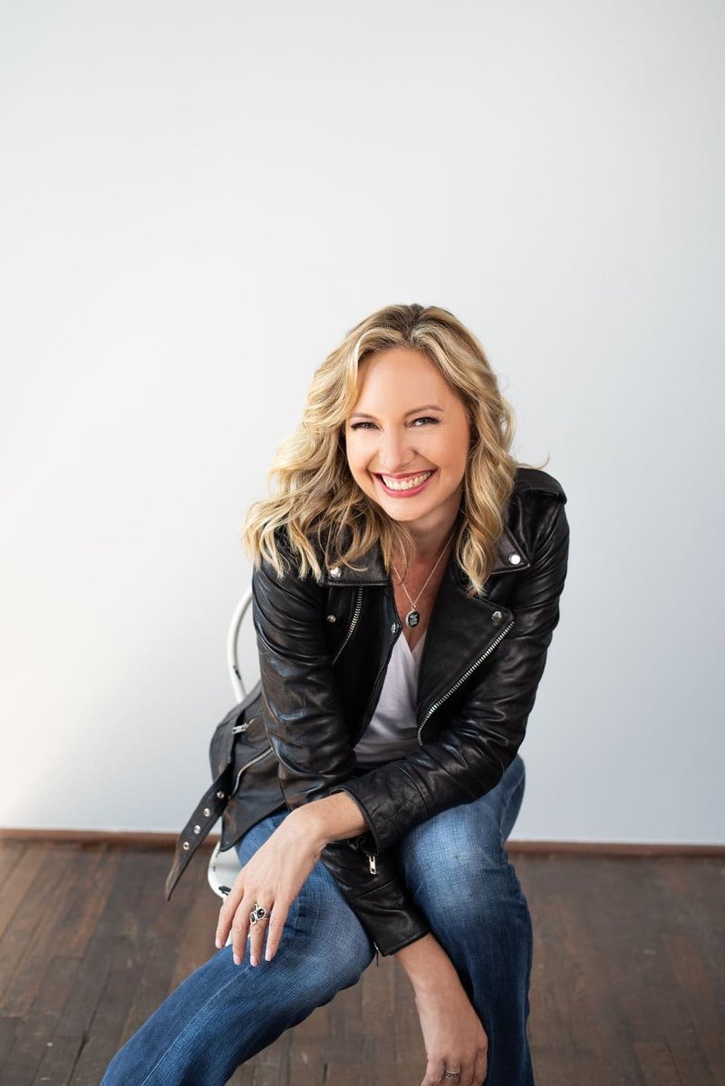 Jen Denton smiling wearing a black leather jacket and jeans