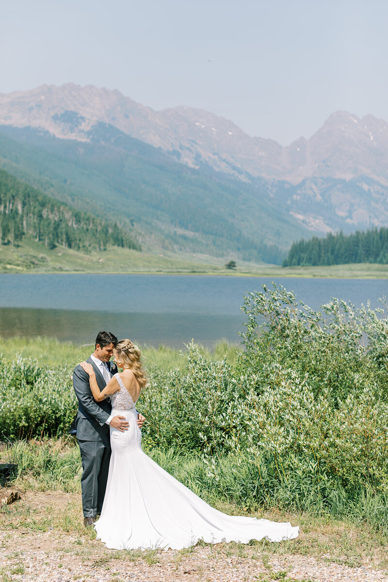 Testimonial photo of bride and groom from a distance. In the background is a lake and mountain range.