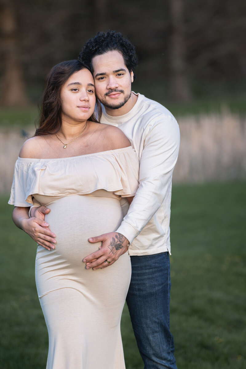 A pregnant couple standing close and holding her stomach.