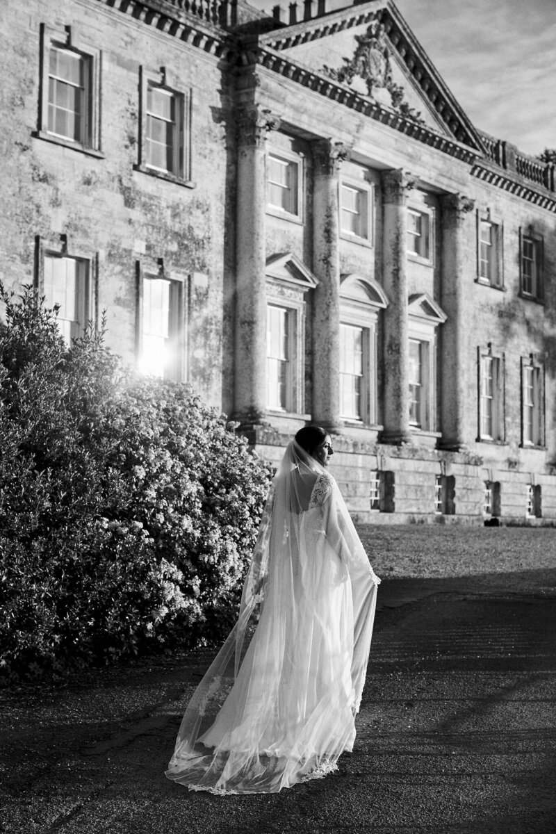 Black and white photo of bride walking past wedding venue manor house