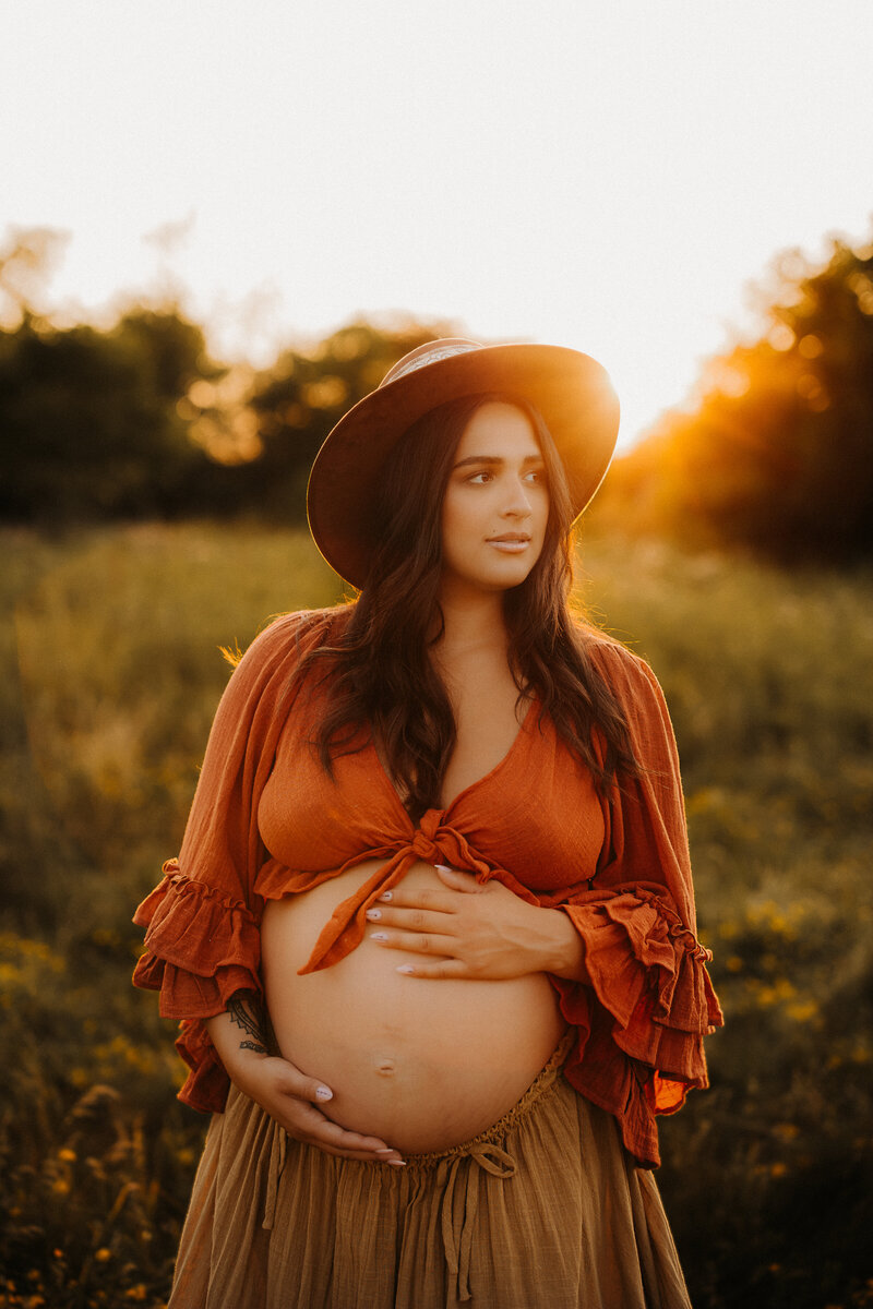 Pregnant mother holding her belly wearing a red crop top and mustard skirt.
