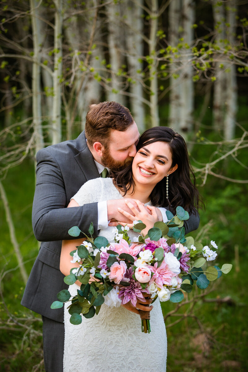 Jackson Hole wedding photographers capture couple hugging before Grand Teton wedding with bride holding pink bridal bouquet