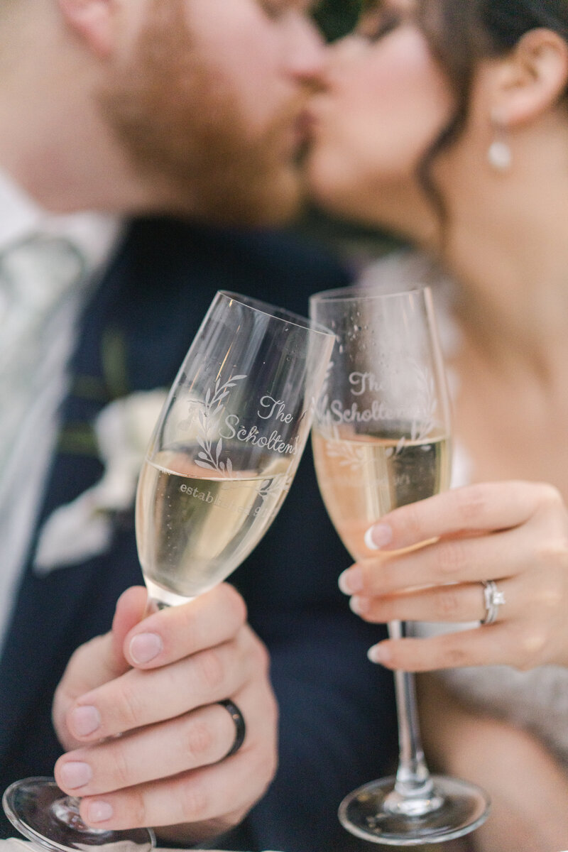 champagne glasses toasting as bride and groom kiss in the background