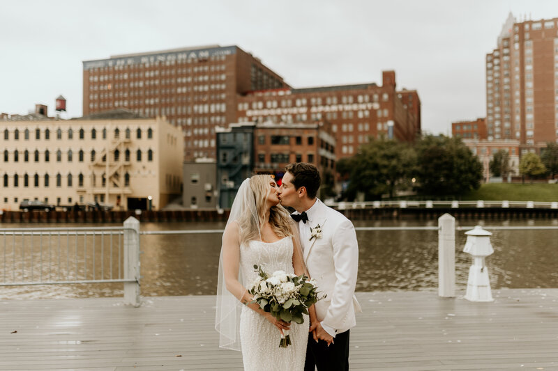 A newlywed couple kisses in front of a lake in the city.