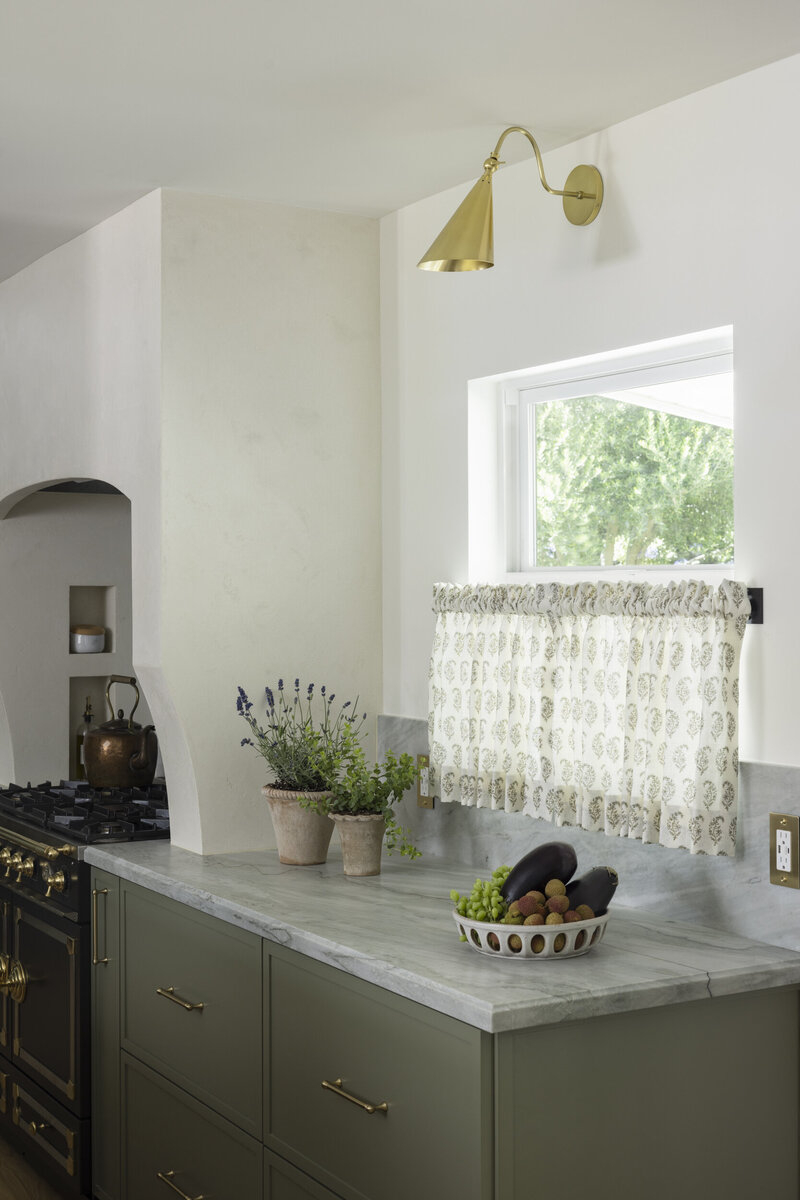 Green cabinets with quartzite countertops and cafe curtains